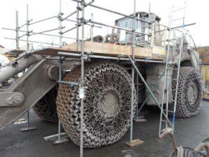 large industrial wheel loader, likely a Cat 992, which has scaffolding erected around its massive wheels for maintenance or inspection.